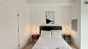 Habitación de hotel con una cama grande, dos mesitas de noche con lámparas, un cabecero y obras de arte en las paredes.