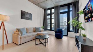Una sala de estar moderna con un sofá, una mesa de centro, un sillón azul, una lámpara de pie y un televisor montado en la pared.