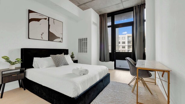 Una habitación de hotel moderna con una cama grande, un escritorio y vistas a edificios a través de la ventana.