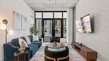Ein modernes Wohnzimmer mit einem blauen Sofa, einem runden Couchtisch und einem wandmontierten Fernseher.