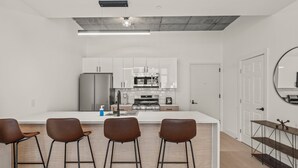 Una cocina moderna con armarios blancos, un refrigerador de acero inoxidable y una isla central con taburetes de bar.