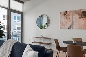 A modern living room with a sofa, a round mirror, a dining table with chairs, and abstract wall art.