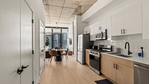 Une cuisine moderne avec des meubles blancs, des appareils en acier inoxydable et un coin repas comprenant une table et des chaises.