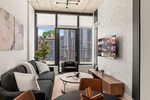 A modern living room with a grey sofa, a round coffee table, and a TV mounted on the wall. - NoLibs Nook | Trendy 1BR Retreat for Group of 4 (Philadelphia)