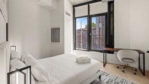 Une chambre moderne avec un grand lit, un bureau et une vue sur la ville grâce à une grande fenêtre.