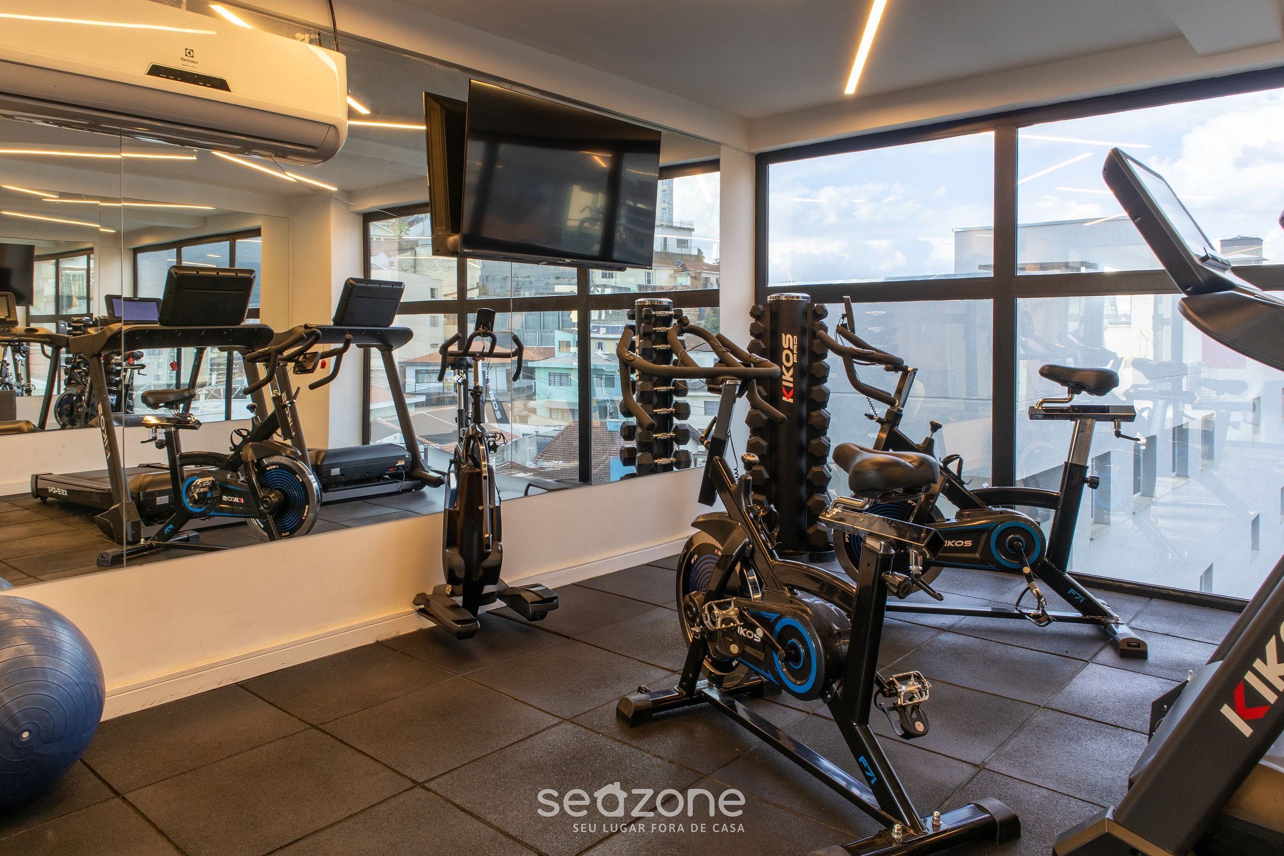 Un gimnasio con diversos equipos de ejercicio, un espejo grande y un televisor en la pared.