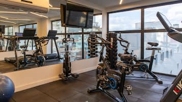 A gym with various exercise equipment, a large mirror, and a TV on the wall.