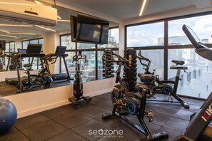 A gym with various exercise equipment, a large mirror, and a TV on the wall. - Your Complete Stay With Pool and gym in Pocos de Caldas - NGO (Poços de Caldas)