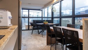 A modern kitchen with a coffee machine, a dining area with a table and chairs, and large windows offering a view of the city. - Your Complete Stay With Pool and gym in Pocos de Caldas - NGO (Poços de Caldas)
