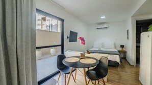 A compact hotel room with a bed, a small table with chairs, a potted orchid, and a TV on the wall. - Your Complete Stay With Pool and gym in Pocos de Caldas - NGO (Poços de Caldas)