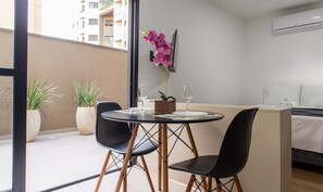 A modern hotel room with a balcony, a dining table with chairs, a small potted plant, and a bed with neatly folded towels.