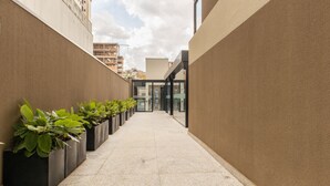 A narrow corridor with potted plants on one side, leading to a building entrance with glass doors. - Your Complete Stay With Pool and gym in Pocos de Caldas - NGO (Poços de Caldas)