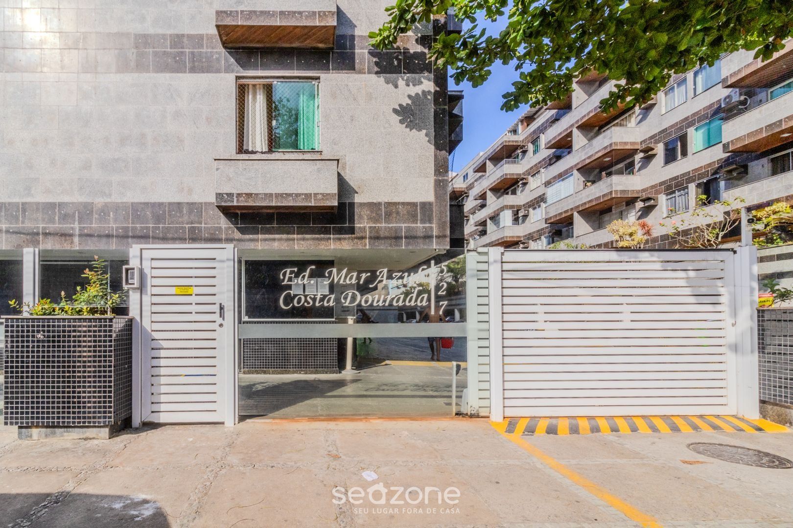 A gated entrance to Ed. Mar Azuleta Costa Dourada, featuring a metal gate and a sign with the property name.