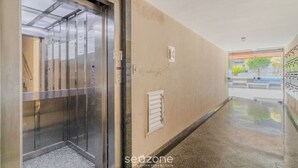 Ein Aufzug in einer Diele mit einer beigen Wand, einem kleinen Fenster und einer Tür zu einem Zimmer.