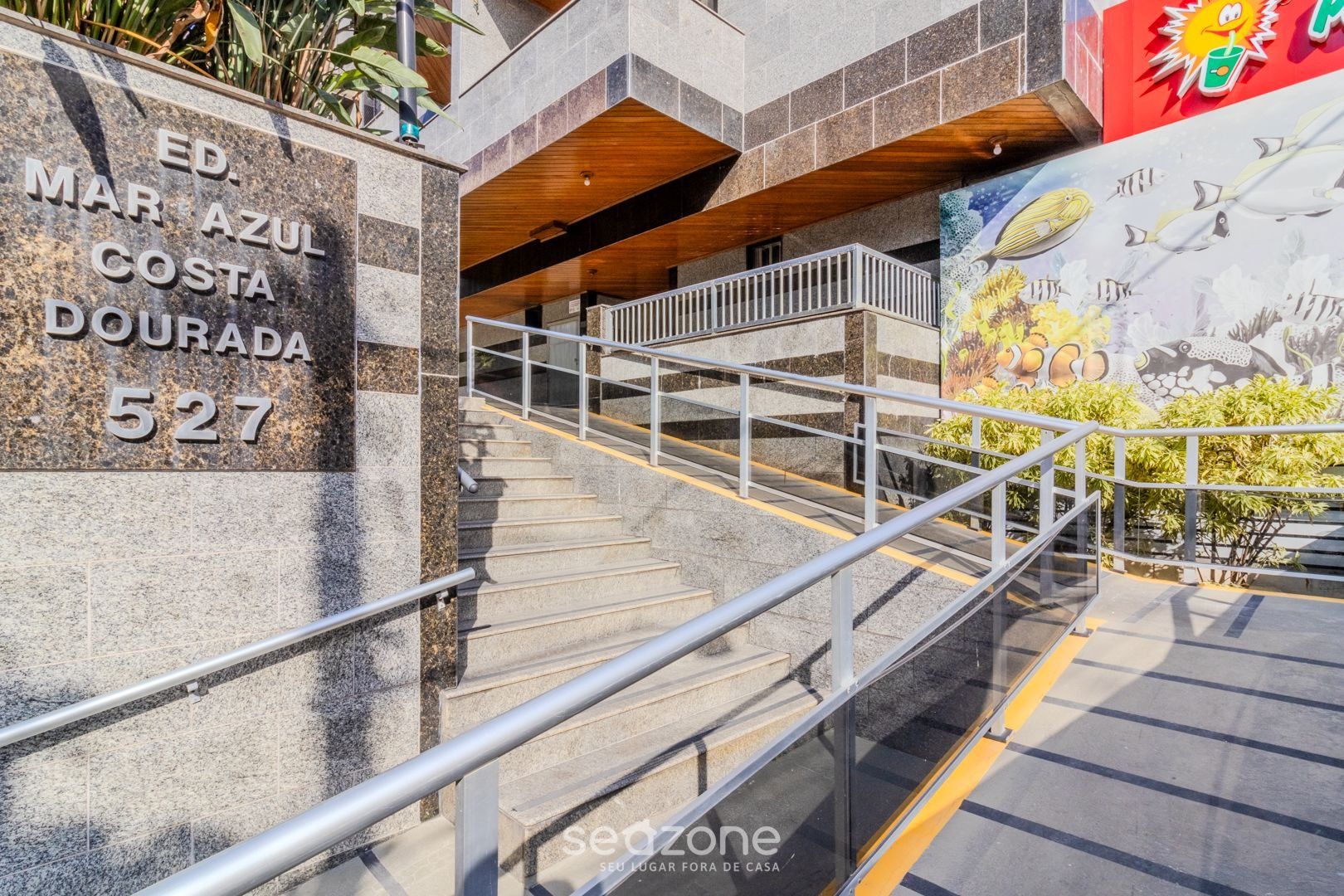 A staircase with metal railings leading to a building entrance. A sign with the address "ED. MAR AZUL COSTA DOURADA 527" is visible.