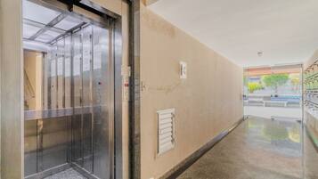 An elevator in a hallway with a beige wall, a small window, and a door leading to a room.