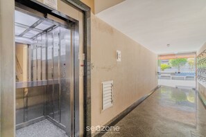 Un ascenseur dans un couloir avec un mur de couleur beige, une petite fenêtre et une porte donnant sur une pièce.
