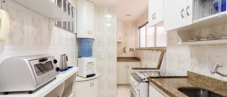 A modern kitchen with white cabinets, a granite countertop, a built-in oven, and a water dispenser.