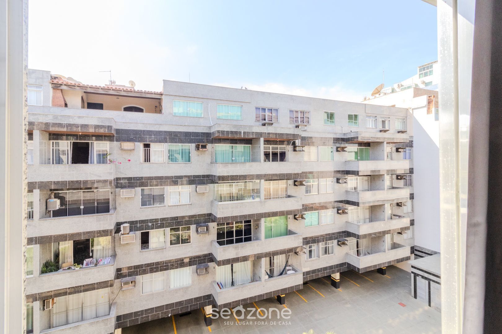 Un edificio residencial de varios pisos con balcones, unidades de aire acondicionado y un área de estacionamiento.