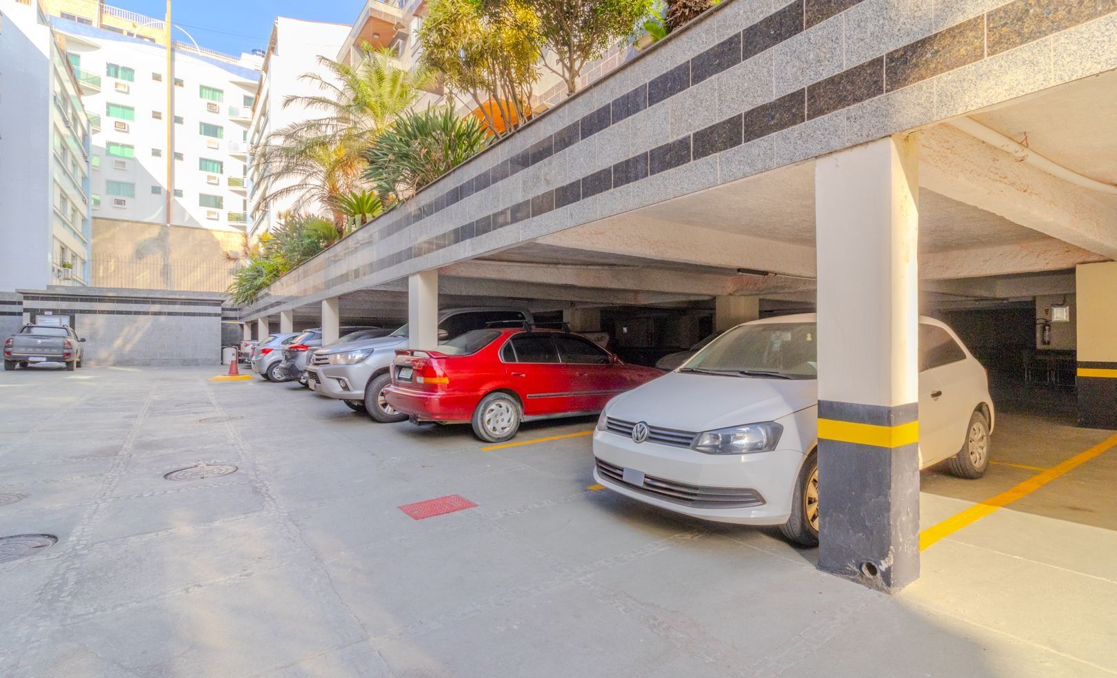Un aparcamiento de varios niveles, con suelos de hormigón y una fila de coches estacionados, incluyendo un sedán rojo y un coche blanco.
