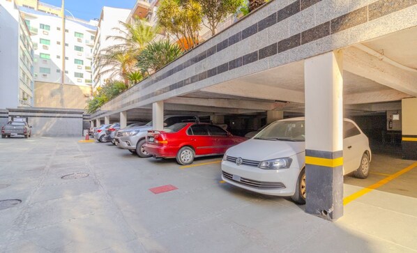 Un parking à plusieurs niveaux, avec des planchers en béton et une rangée de voitures garées, dont une berline rouge et une voiture blanche.