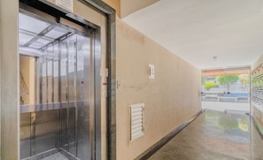 An elevator in a hallway with a beige wall, a small window, and a door leading to a room. - Comfortable Apartment 50m From Forte Beach Mzd0308 (Cabo Frio)