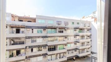 Un edificio residencial de varios pisos con balcones, unidades de aire acondicionado y un área de estacionamiento.