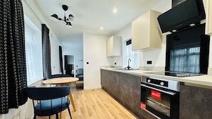 A modern kitchen with a wooden floor, a dining area with a table and chairs, and a built-in oven. - Rhode Lane Serviced Apartments (Bridgwater)