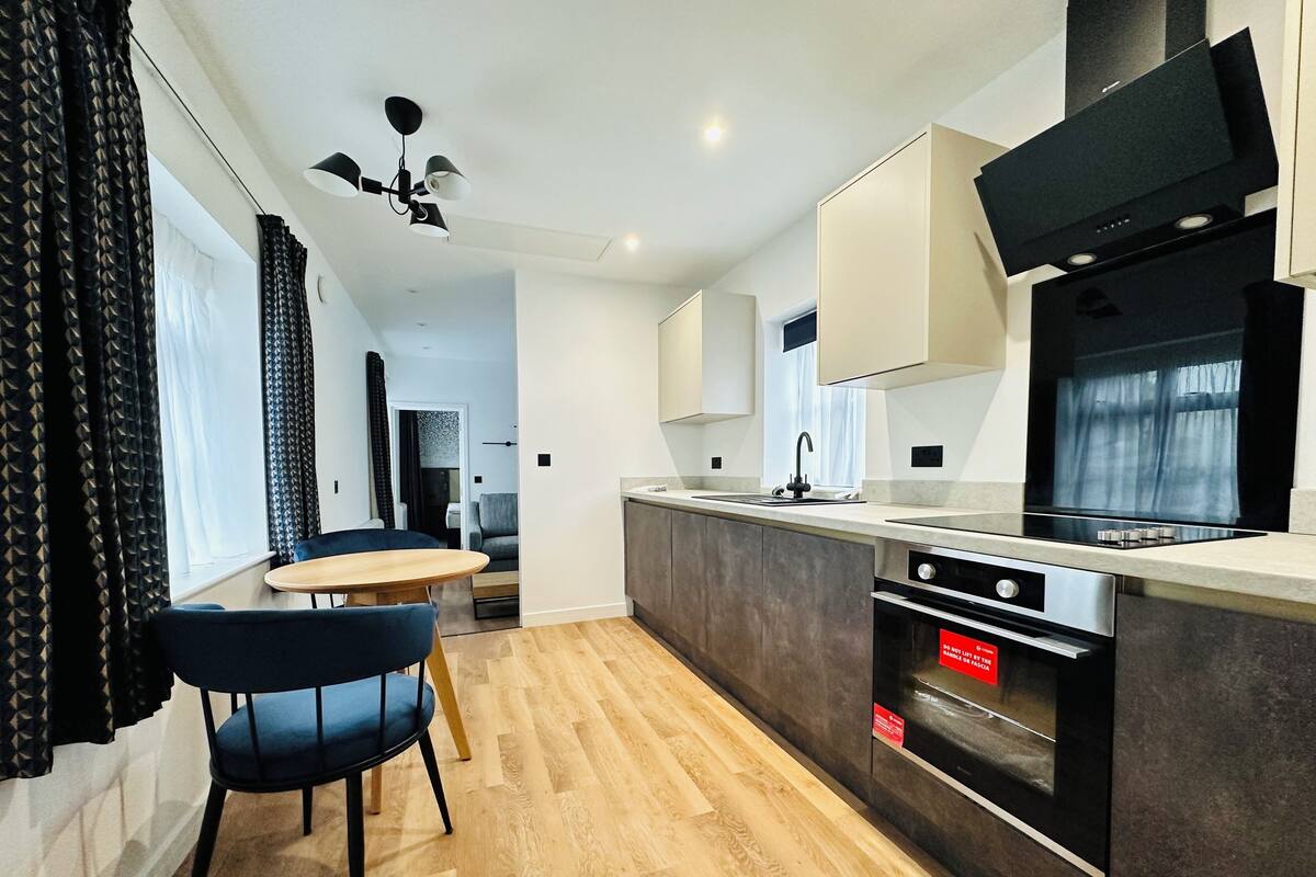 Cozinha moderna com piso de madeira, área de refeições com mesa e cadeiras, e forno embutido.