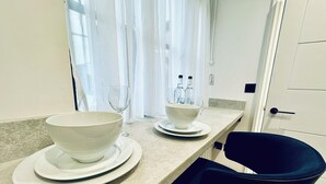A kitchen counter with two white bowls on plates, a wine glass, and two bottles of water. - Rhode Lane Serviced Apartments (Bridgwater)