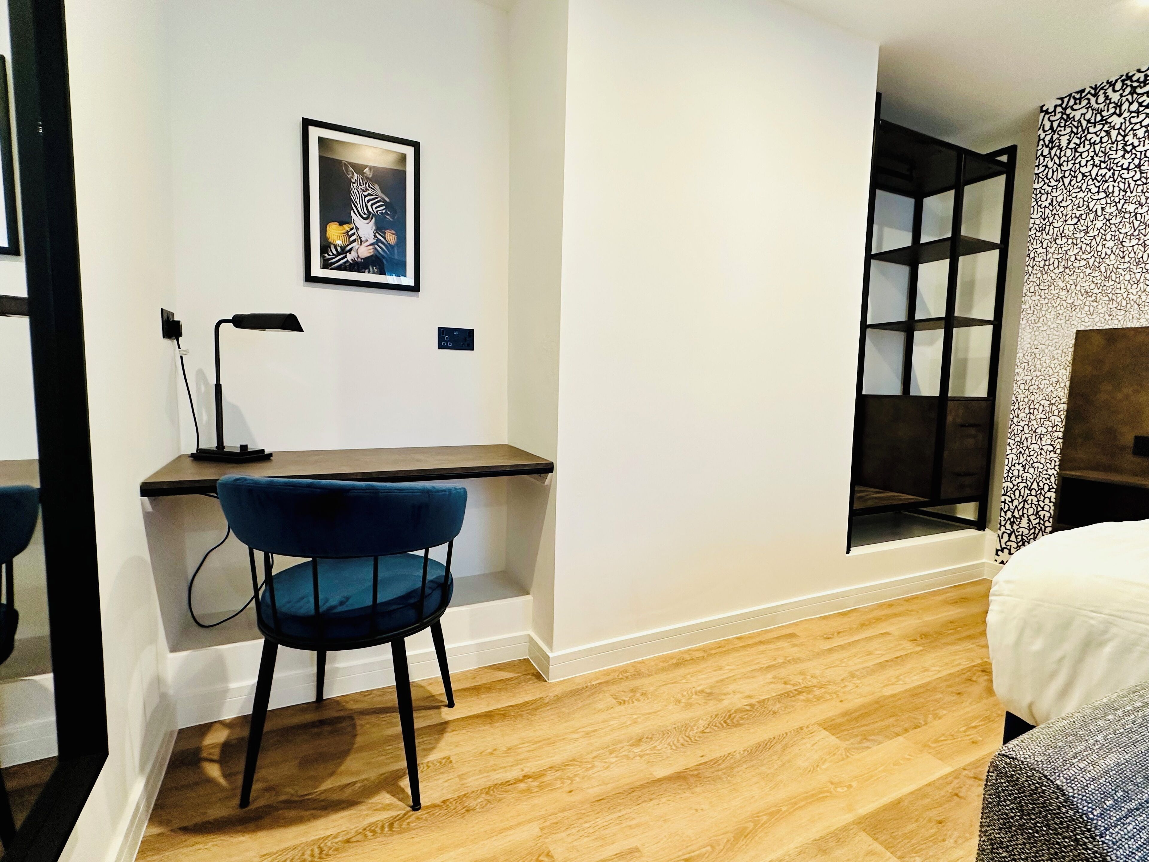 A modern bedroom with a wooden desk, a blue chair, a bed, and a large window with a view.