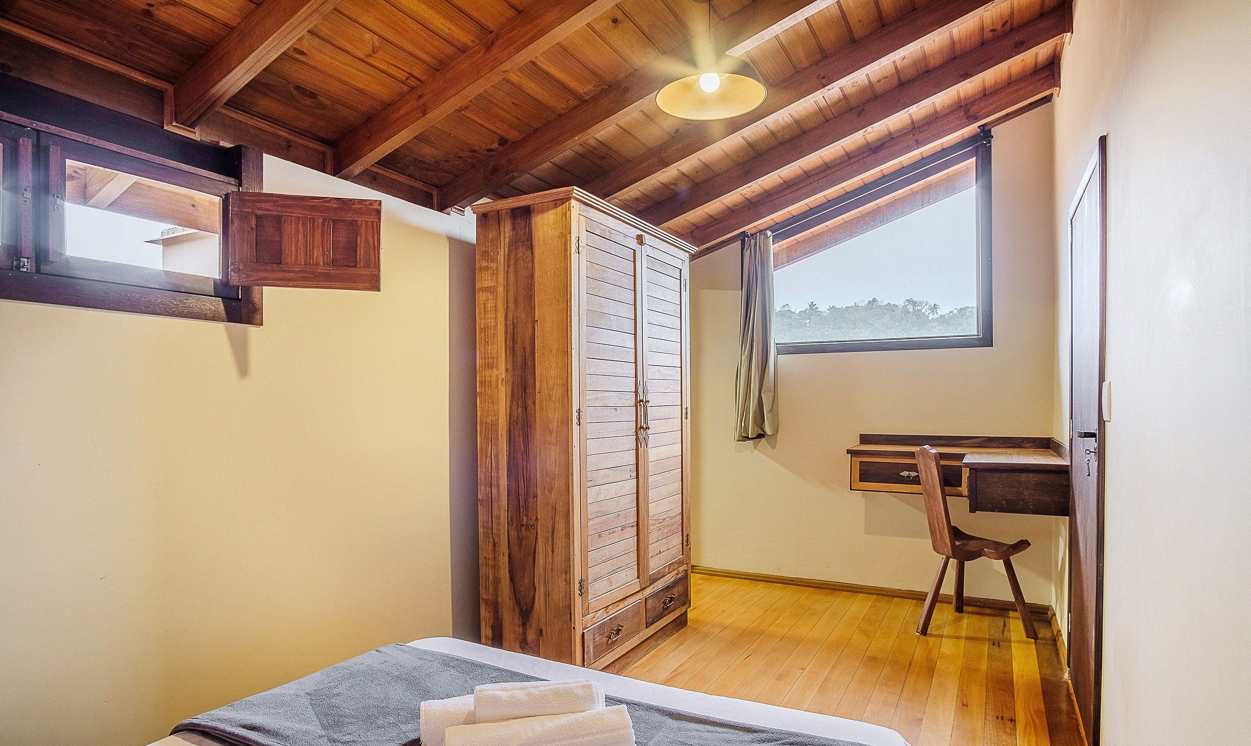 Ein Zimmer mit Holzbalkendecke, einem Kleiderschrank, einem Schreibtisch und einem Fenster mit Blick.