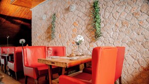 Ein Restaurant mit roten Ledersitzbänken, einem Holztisch gedeckt mit Tellern, Gläsern und einer Blumenvase.