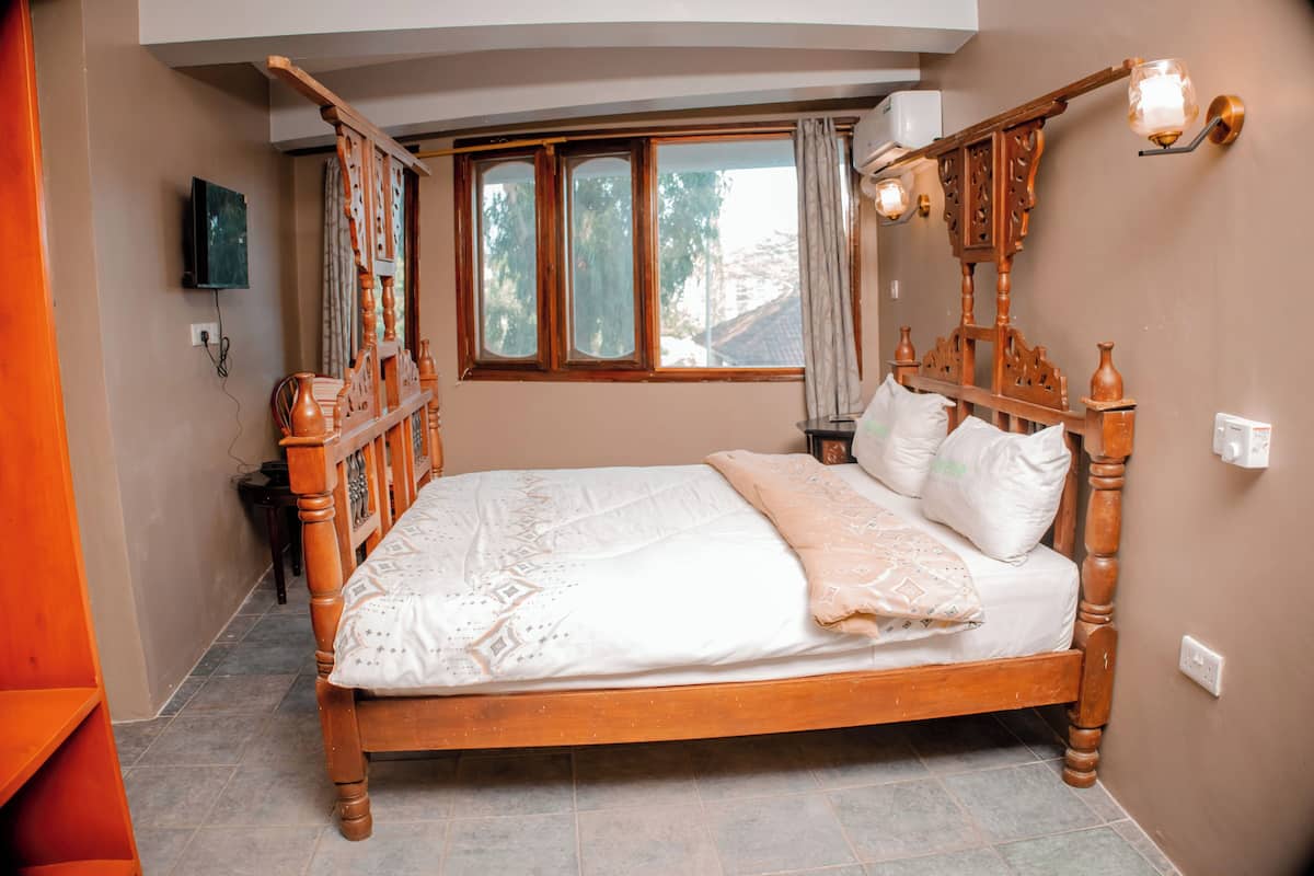 A wooden four-poster bed with a white bedspread and pillows, a window with curtains, and a wall-mounted light fixture.