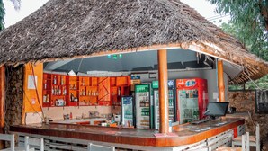 Eine Bar mit einem Strohdach, Holzböden mit Flaschen und einem Kühlschrank.