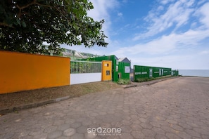 A paved walkway leading to a gated area with green and yellow fencing, a clear sky, and a body of water in the background. - Charming House With BBQ by the sea Mon0099 (Barra Velha)