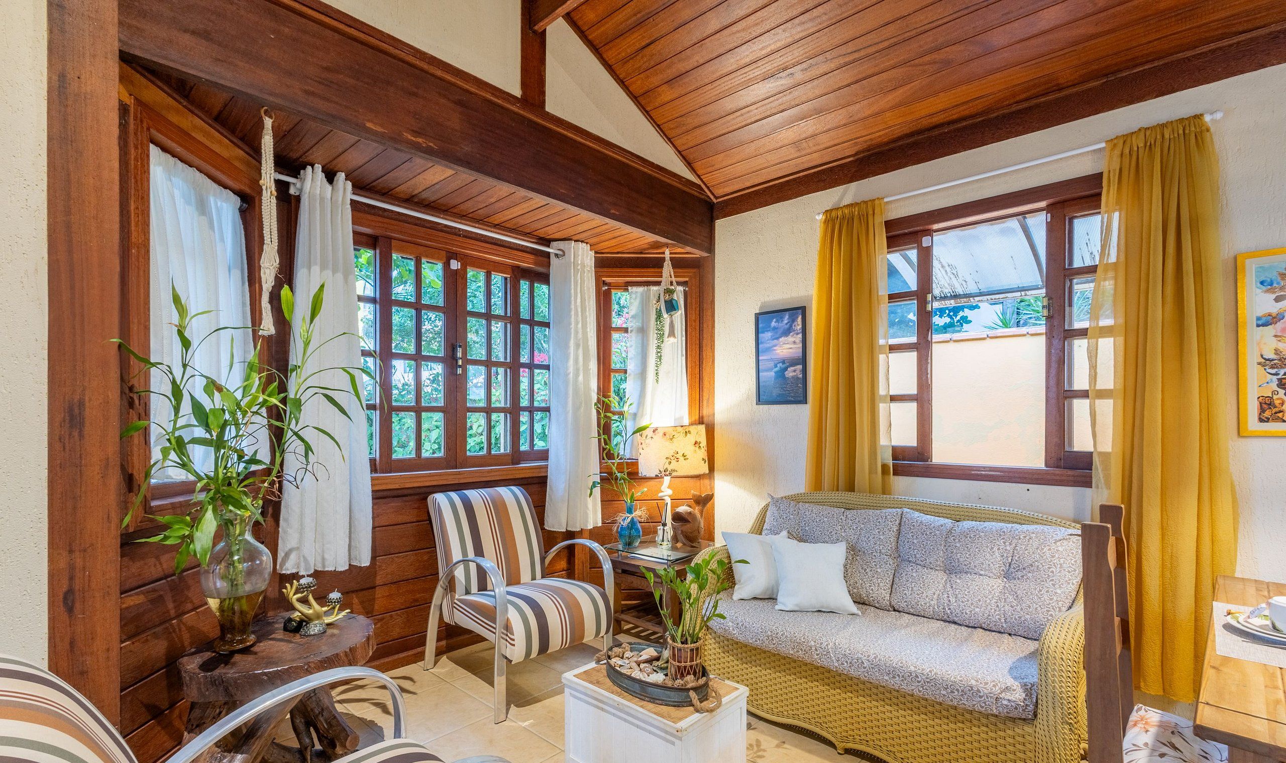 A cozy room with a wooden ceiling, a sofa, a dining table, and a window with curtains.