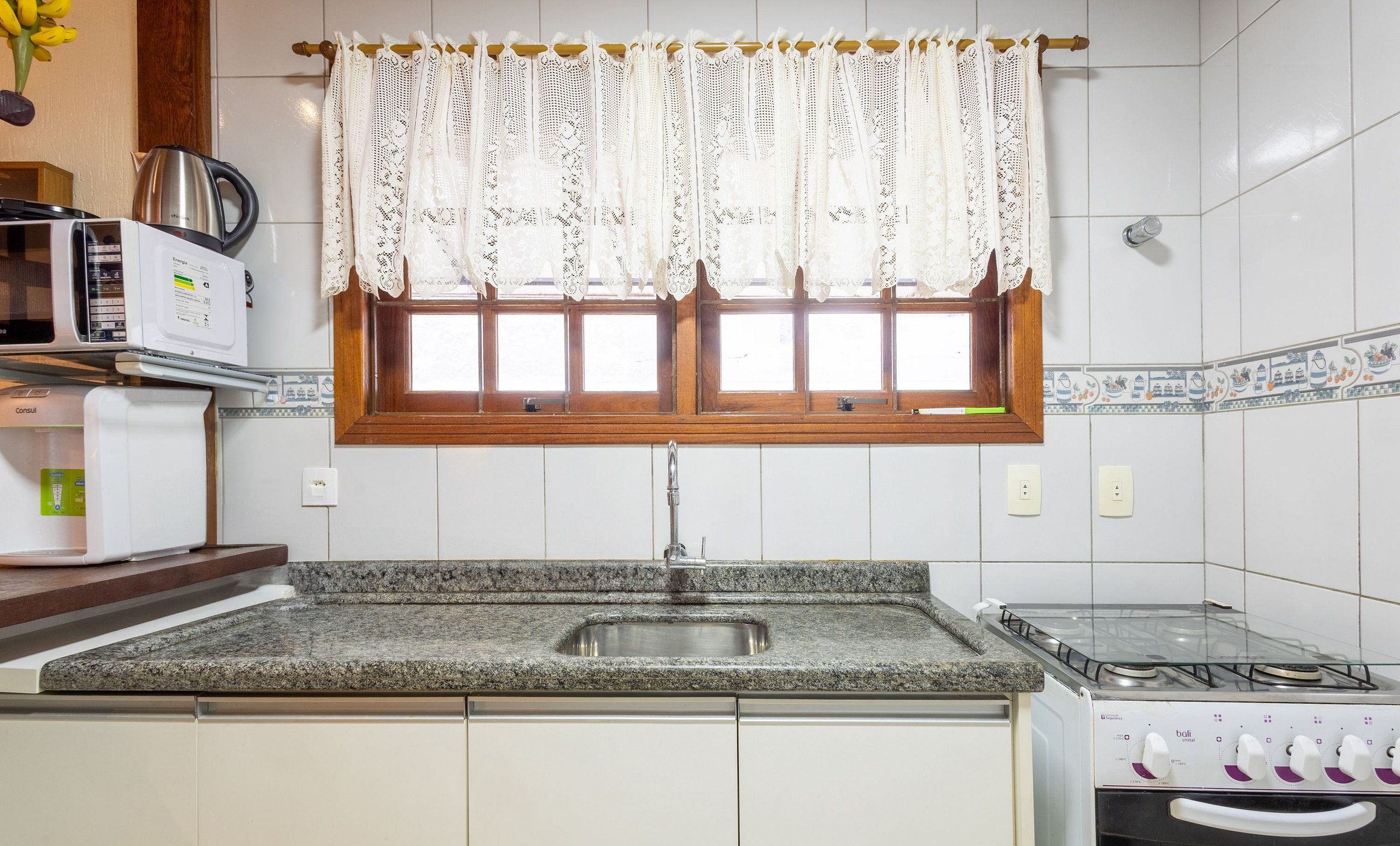 A kitchen with a granite countertop, a stainless steel sink, a stove, and a microwave.