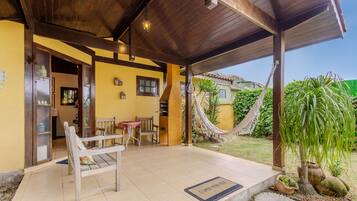 A covered outdoor seating area with wooden chairs and a table, a hammock, and a doormat with a message.