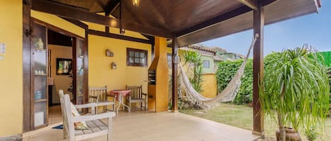 A covered outdoor seating area with wooden chairs and a table, a hammock, and a doormat with a message.