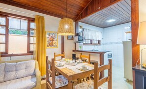 A cozy dining area with a wooden table and chairs, a wicker hanging light fixture, and a view of the kitchen through a window with yellow curtains. - Charming House With BBQ by the sea Mon0099 (Barra Velha)