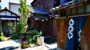 Ein traditionelles japanisches Gebäude mit Holzbauweise, einem Ziegeldach und einem kleinen Garten mit einem Wegweiser.