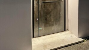 Eine moderne, metallische Tür mit Griff und einer kleinen Stufe davor, an einer schlichten Wand.