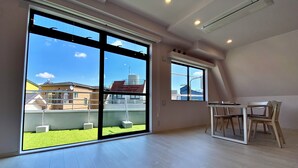 Ein geräumiger Raum mit großen Schiebeglasüren zum Balkon, einem Esstisch mit Stühlen und einer Decke mit Einbaustrahlern.