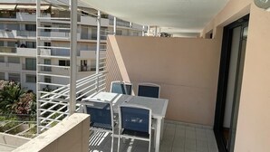 Un balcon avec une table et des chaises, une rambarde en métal et une vue sur les bâtiments voisins.