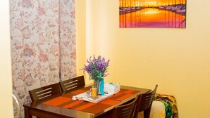 Ein Essbereich mit Holztisch, Stühlen, einer Blumenvase, einem Tablett mit Gewürzen und einem Gemälde an der Wand.