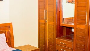 Ein Schlafzimmer mit einem Holzschrank, einem Bett mit einem rosafarbenen Kissen und einem kleinen Nachttisch.