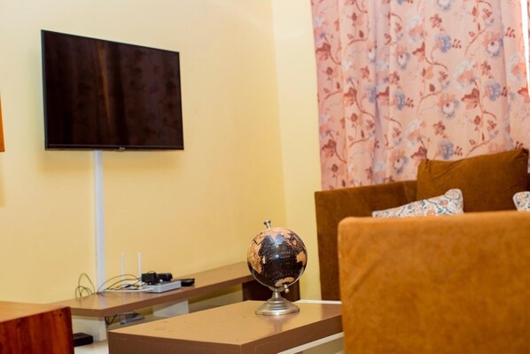 A room with a flat-screen TV mounted on the wall, a globe on a table, and a sofa with patterned cushions.