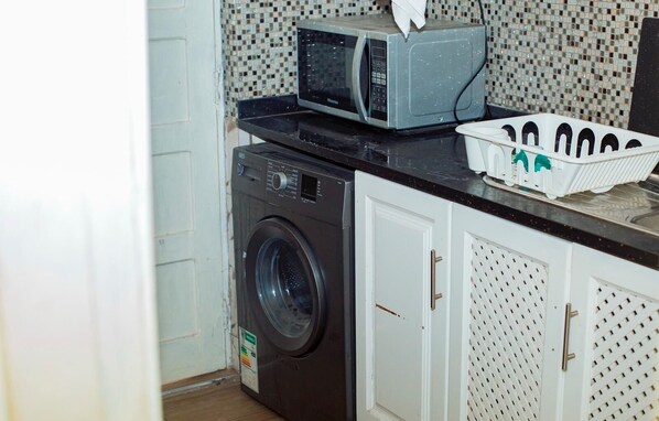 A compact laundry area with a washing machine, a microwave, and a drying rack.