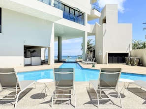 A pool area with lounge chairs and a view of the ocean.
